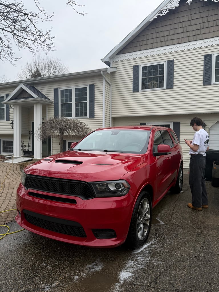 Red Dodge Durango SUV parked in driveway of white colonial home with person standing beside vehicle
