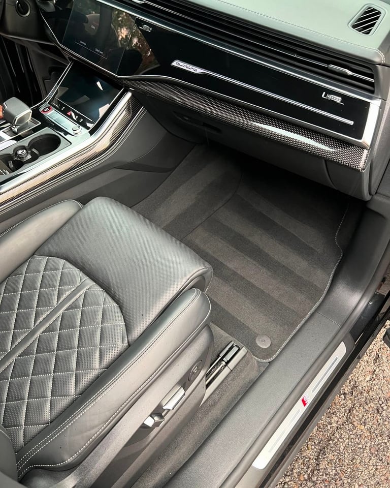 Interior view of luxury car showing quilted leather seat, black floor mat, and modern dashboard with climate controls