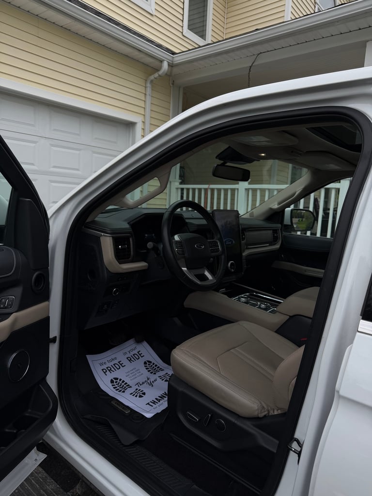 Interior view of white truck cab with open driver door, beige seats, steering wheel, and residential garage in background