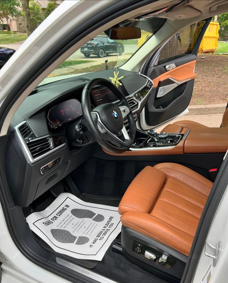 Interior view of a luxury SUV with brown leather seats, dark steering wheel, and digital dashboard, parked in a driveway