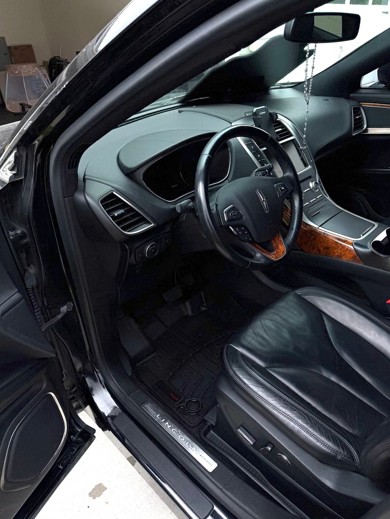 Interior view of luxury car with steering wheel, dark leather seats, and wood grain trim visible through open driver door